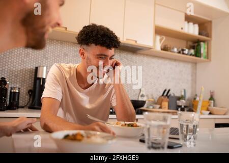 Happy young man eating and using laptop in kitchen Stock Photo