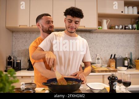 Affectionate gay male couple cooking in kitchen Stock Photo