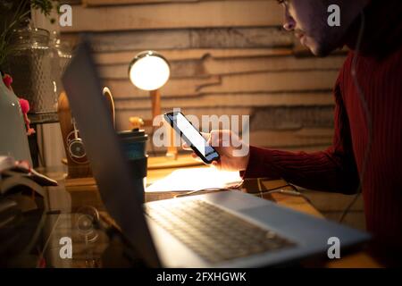 Young man using smart phone at laptop in home office Stock Photo