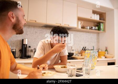 Gay male couple eating and using laptop at kitchen counter Stock Photo