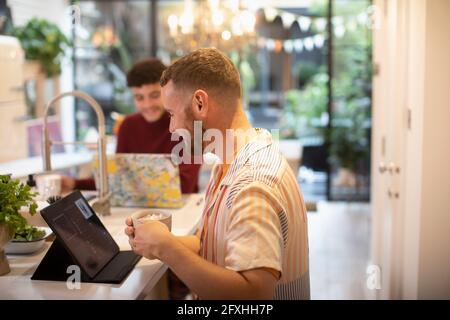 Gay male couple using digital tablet and laptop in kitchen Stock Photo