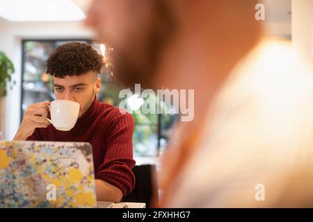 Young man drinking coffee working from home at laptop Stock Photo