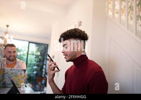 Young man talking on smart phone speaker in kitchen Stock Photo