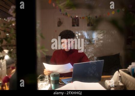 Focused young man with paperwork working from home at laptop at night Stock Photo