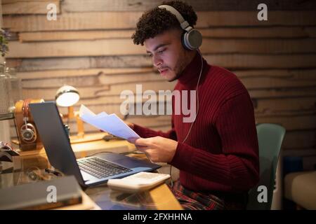 Young man with headphones and paperwork working late at home Stock Photo