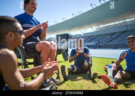 Paraplegic and amputee male athletes clapping on sunny stadium grass Stock Photo