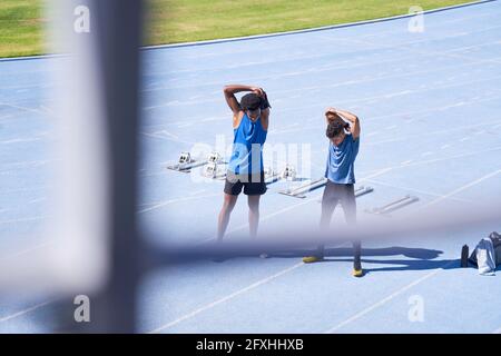 Male runners stretching on sunny blue sports track Stock Photo