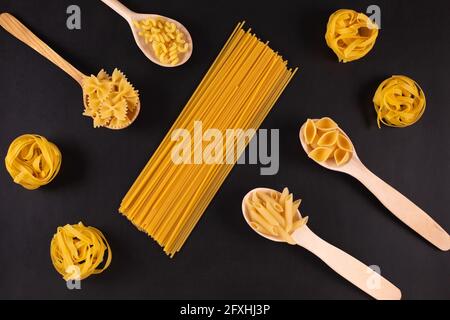 Different pasta types in wooden spoons on black table. Top view. Stock Photo