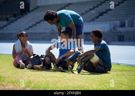 Happy athlete friends resting and talking on sunny stadium grass Stock Photo