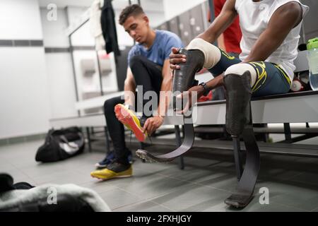 Male amputee athlete adjusting running blade prosthetic in locker room Stock Photo