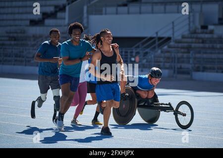 Happy diverse athletes running on sunny sports track Stock Photo