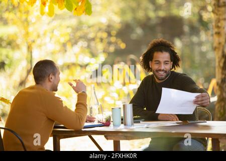 Businessmen discussing paperwork at table in autumn park Stock Photo