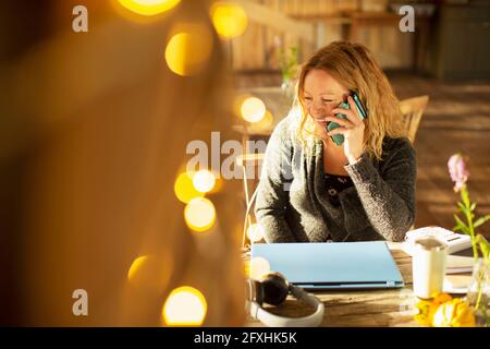 Happy businesswoman talking on smart phone in sunny cafe Stock Photo
