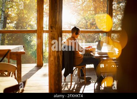 Businessman with headphones working at laptop in sunny cafe Stock Photo