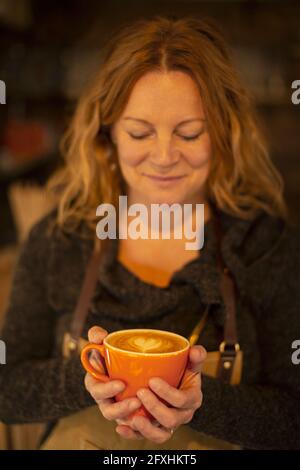 Happy female barista holding cappuccino with heart shape foam Stock Photo