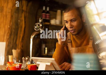 Male cafe owner taking order by phone at digital tablet Stock Photo