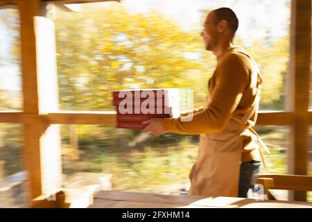 Male pizzeria owner carrying pizza boxes along sunny autumn window Stock Photo