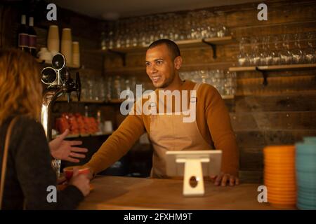 Friendly barista talking with customer at cafe counter
