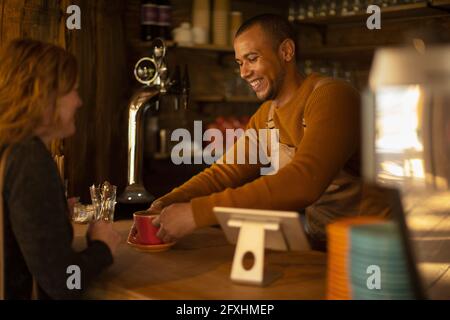 Friendly barista serving coffee to excited woman at cafe counter Stock Photo