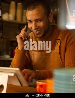 Smiling male barista taking order by phone at digital tablet in cafe Stock Photo