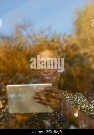 Smiling woman using digital tablet at sunny autumn window Stock Photo