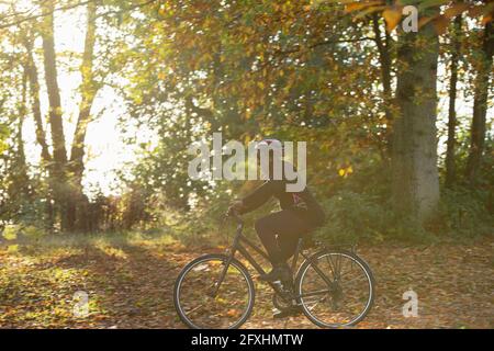 Happy woman bike riding among autumn leaves in sunny park Stock Photo