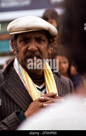 A man wearing a light-coloured flat cap and a yellow scarf watches the flamenco concert on the café terrace in Saintes-Maries-de-la-Mer, his hands clasped. Roma pilgrimage, May 1978. Saintes-Maries-de-la-Mer, Arles, Bouches-du-Rhône, Provence-Alpes-Côte d'Azur, 13460, France Stock Photo