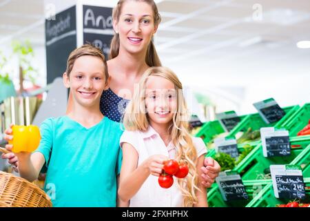 Mother and children selecting vegetables while grocery shopping in organic supermarket Stock Photo