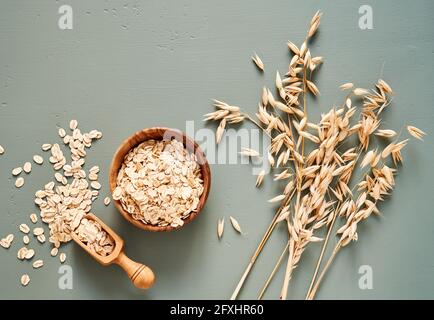 Oat flakes in wooden bowl and ears of oat on blue background. Flakes for oatmeal and granola. Stock Photo