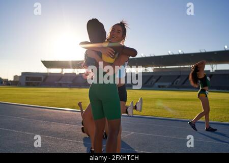Happy female track and field athletes hugging on sunny track Stock Photo