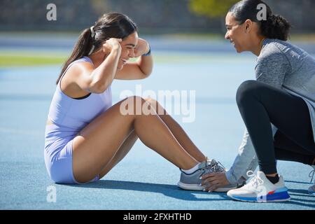 Happy female track and field athletes doing sit ups on track Stock Photo