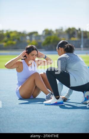 Female track and field athletes doing sit ups on sunny track Stock Photo