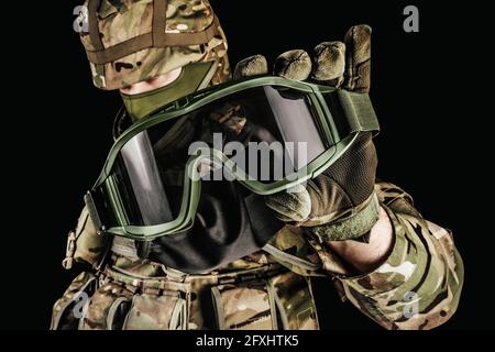 Photo of soldier in level 3 armored vest ammunition, tactical gloves holding tactical goggles on black background. Stock Photo