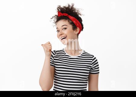 Hey wanna come, check this out. Smiling brunette woman inviting you, pointing thumb behind and looking friendly, beckon to look there, standing over Stock Photo