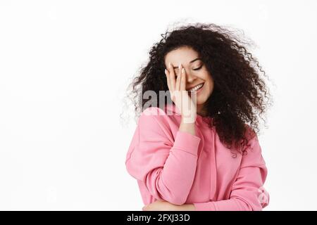 Beauty and lifestyle. Happy brunette woman with dreamy emotion, touching her face and smiling flirty, standing against white background Stock Photo