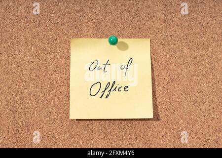Yellow note with phrase out of office on cork board Stock Photo