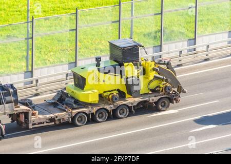 Truck with a long trailer platform for transporting heavy machinery, loaded tractor without wheels and bucket. Highway transportation Stock Photo
