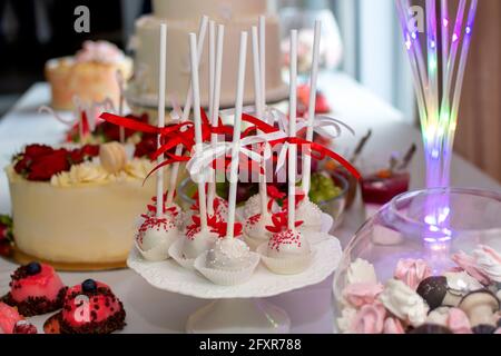 Pops on the wedding table. Pops in white chocolate decorated with red and white ribbons. Sweet wedding table Stock Photo