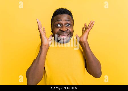 Surprised young african american man in yellow casual t-shirt spreading hands keep mouth and eyes open isolated on yellow background studio portrait Stock Photo