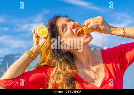 Portrait of happy woman eating and holding lemon slices in red t-shirt. Stock Photo