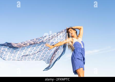 Stylish beautiful female waving towel in the wind .Sunny summer day with blue sky. Stock Photo