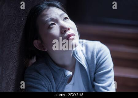 young beautiful Asian woman in pain suffering depression - dramatic indoors portrait on staircase of sad and depressed Korean girl as victim of bullyi Stock Photo