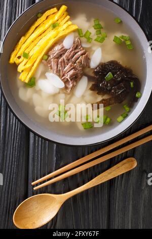 Hearty and comforting Korean rice cake soup Tteokguk closeup in the bowl on the table. Vertical top view from above Stock Photo