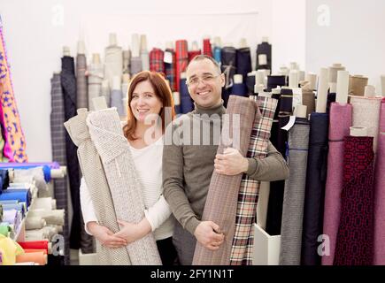 Family business team working together. Couple of two professional tailors holding rolls of fabrics cloth in atelier. Atelier or drapery store owners couple at working place. High quality photo Stock Photo