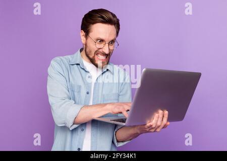 Photo of unhappy angry young man look hold laptop write letter work isolated on purple color background Stock Photo