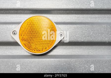 Close up of a round plastic yellow reflector attached to a trailer corrugated metal side. Stock Photo