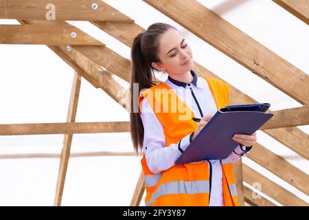 Female architect inspecting the place. Young student engineer close up. Young woman checking and noting the measures on the roof. Stock Photo