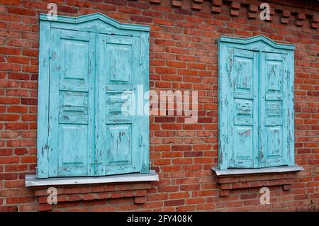 Two windows in old wall with closed blue shutters. Red brick wall. Facade of ancient house. Windows with closed old blue wooden shutters Stock Photo