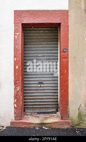 Metal shuttered doorway with red painted surround and worn stone doorstep Stock Photo