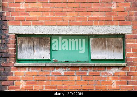 Three boarded up windows set in red brick wall Stock Photo